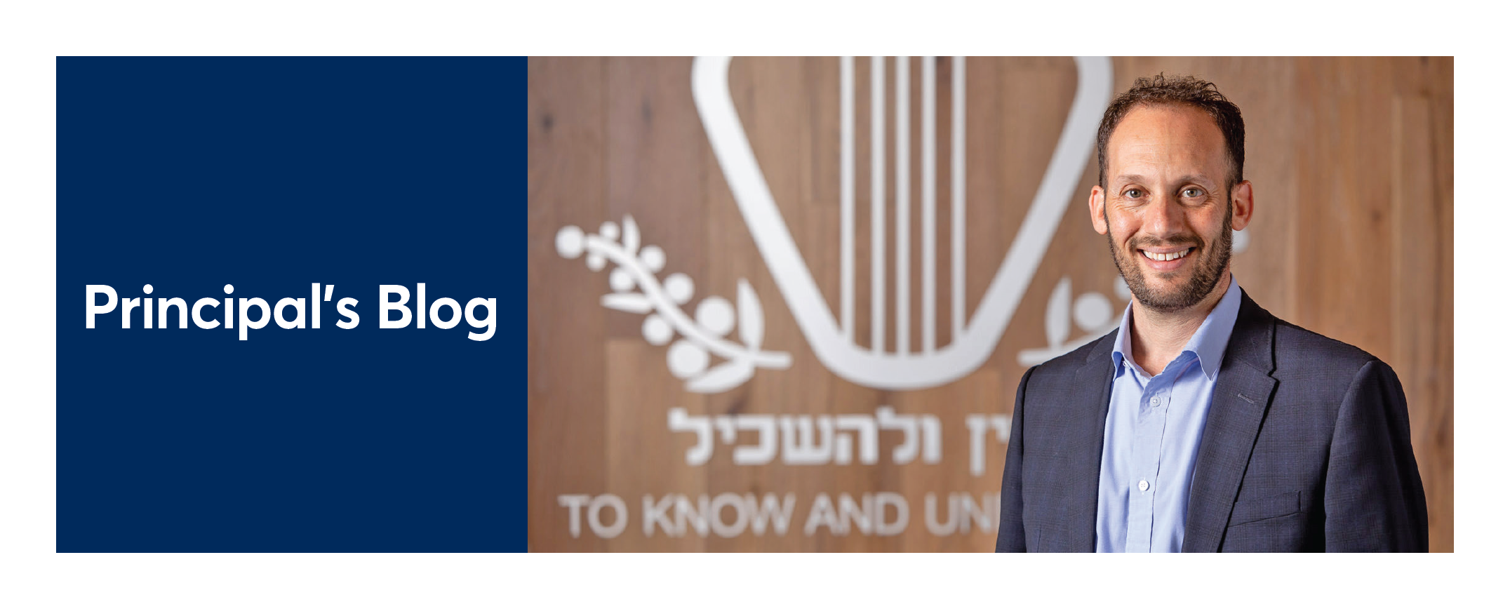 Principal Marc Light looks at the camera, he is wearing a grey suit and smiling. The King David School's logo is behind him, silver on a wood background.