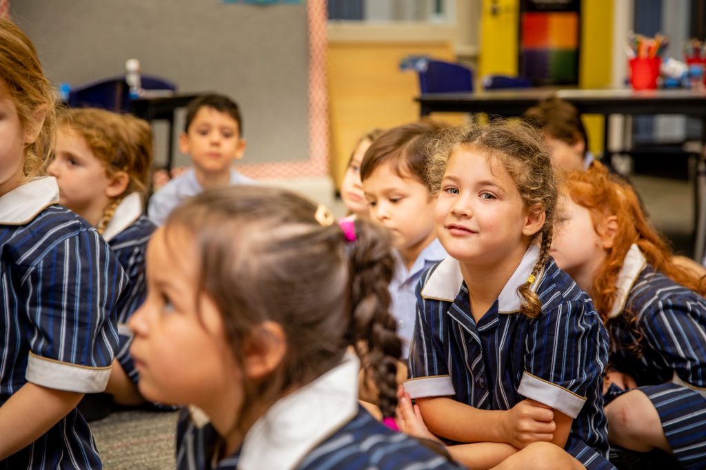 Prep students in the Prep classroom. One girl in plaits looks at the camera and smiles.