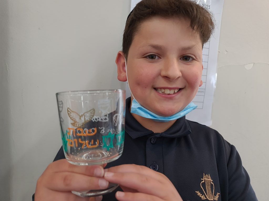 Smiling student holds kiddush cup he decorated himself