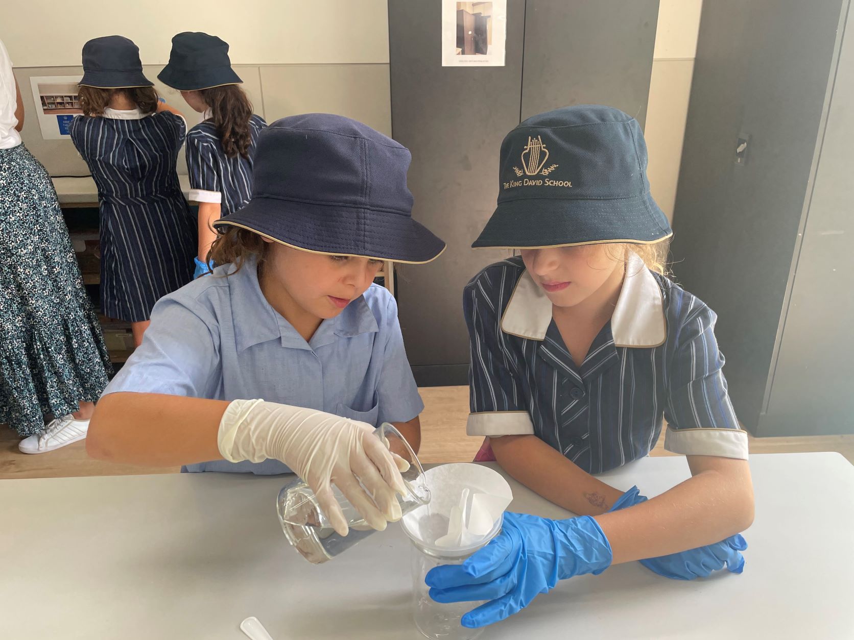 Two Junior School students gaze at plastic receptacle, they are wearing medical gloves and one is holding the receptacle.