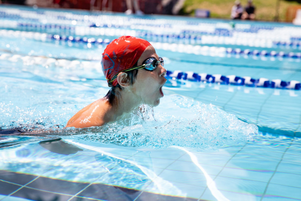 Senior school student wearing a red swimming cap and goggles in a swimming pool splashing water