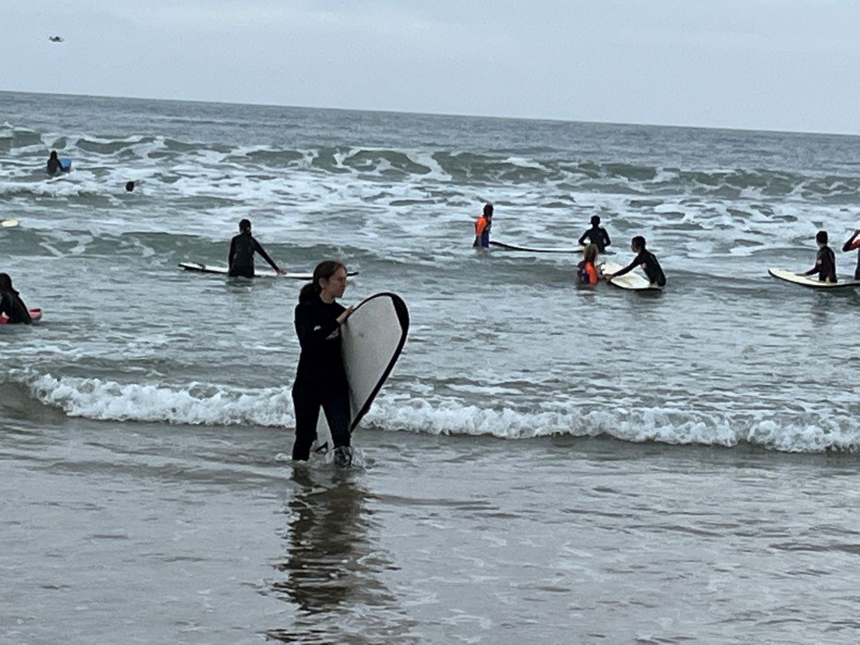 Students in the sea with surfboards, one student is in the middle of the image, standing up with a surfboard
