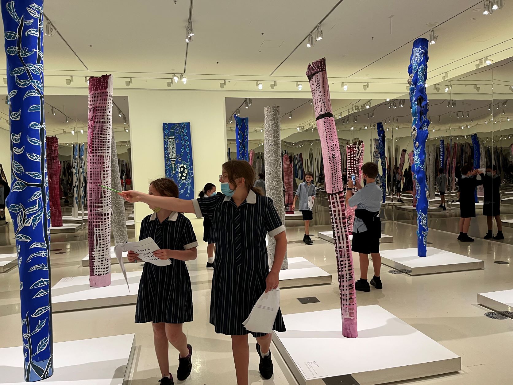 Year 6 students look at First nations art, one student points to a tall pole covered in blue material