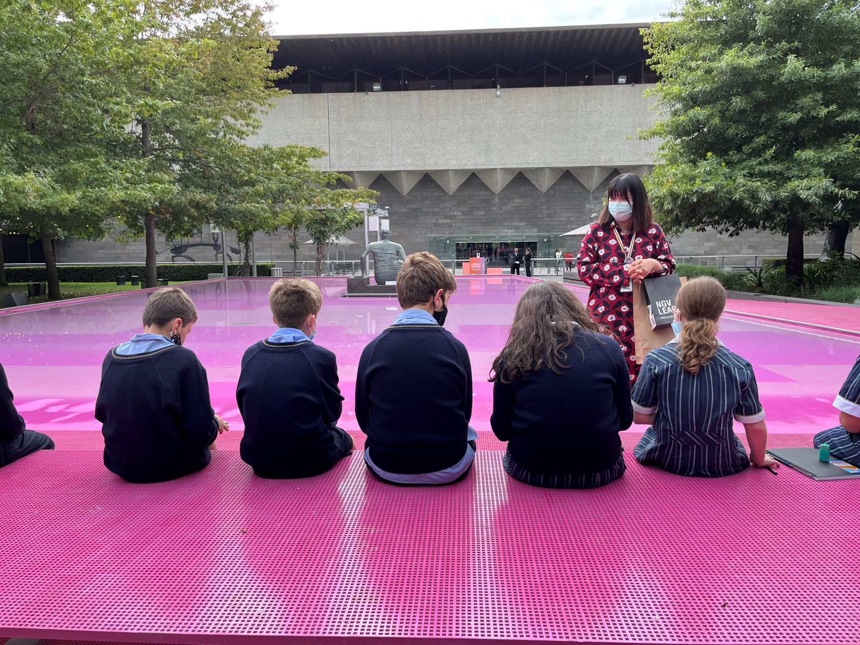 Five students have their back to the camera. They are at the pink lake at the NGV on an art excursion