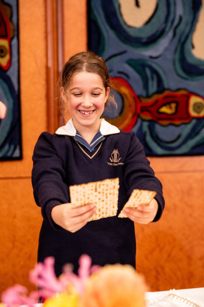 A Junior School student breaks the matzah for the afikoman, looking down excitedly at the matzah