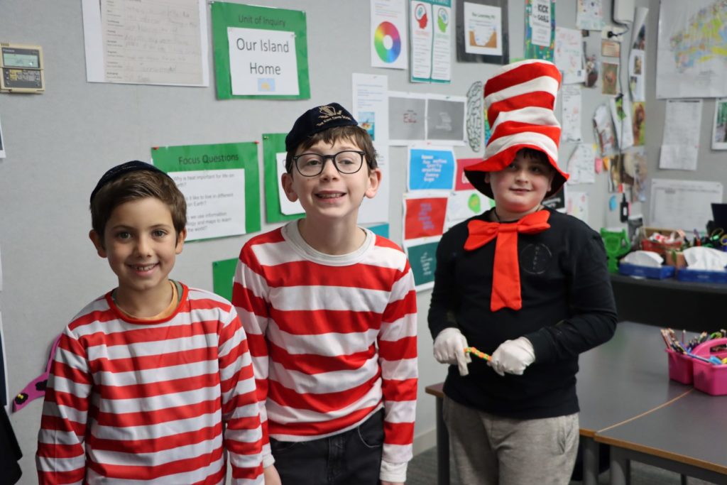 Three Junior School students wearing red and white stripes are looking at the camera and smiling. Two look like Wally from Where's Wally, one student is wearing a tall striped hat like the Cat from the Cat and the Hat by Dr Suess