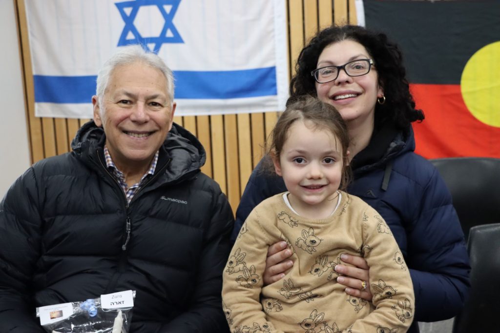 A grandfather, mother and ELC student are celebrating Shabbat together. They are looking at the camera and are happy.