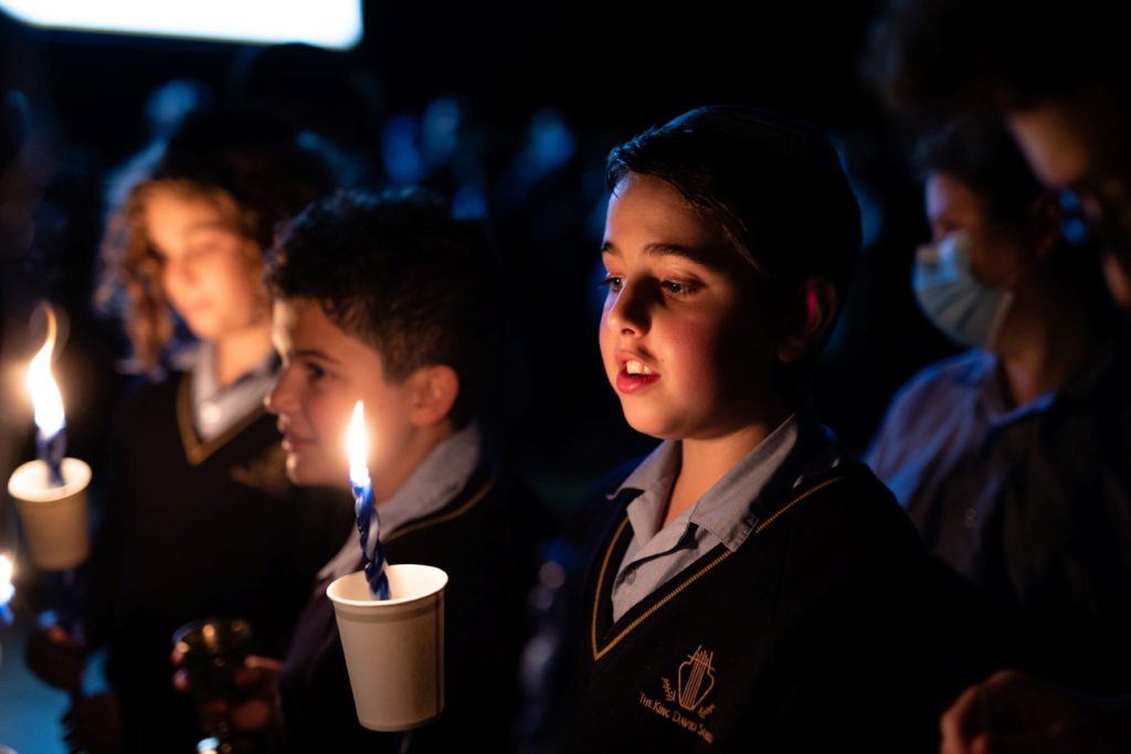Two students hold Havdalah candles. They are looking down at the candle flames with their mouths open, singing a Havdalah song.