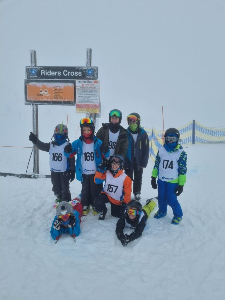 Seven students stand in snow, they are dressed in snow gear and are looking at the camera smiling