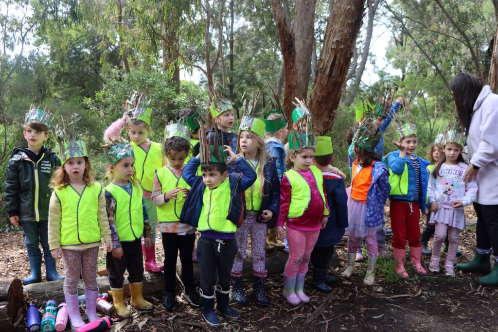 ELC students are in the forest in a group. They are wearing crowns they have made themselves.