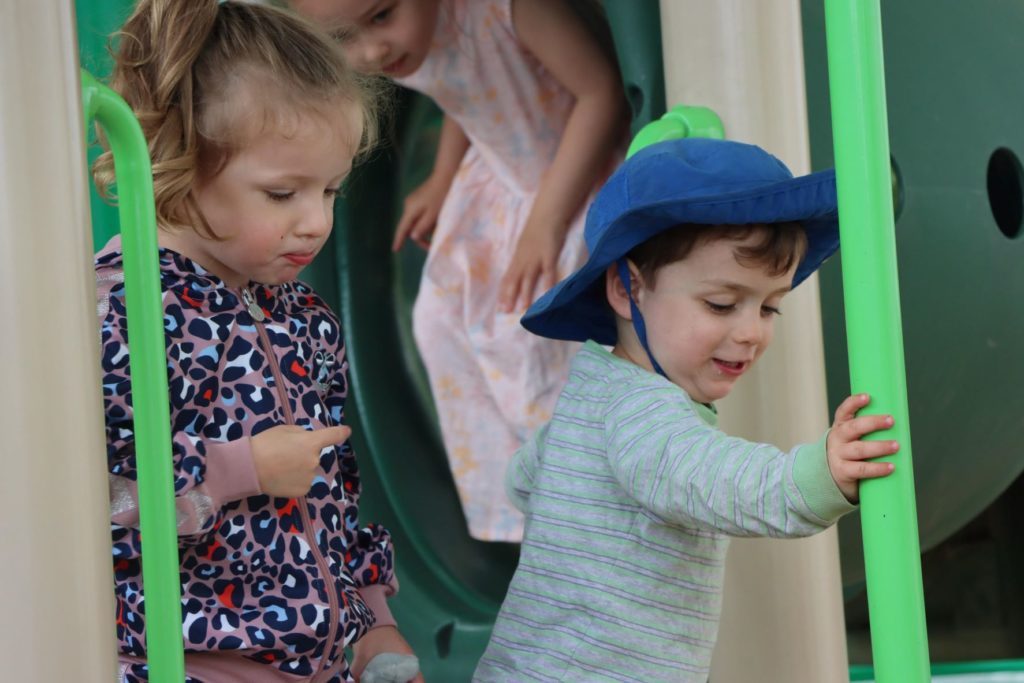 Three ELC students enjoy our playground. They are looking at the play equipment in concentration.