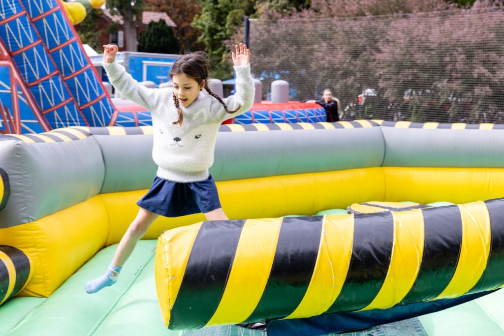 A young girl is playing on a green and yellow inflatable ride at the King's Carnival. She has her arms in the air and is smiling