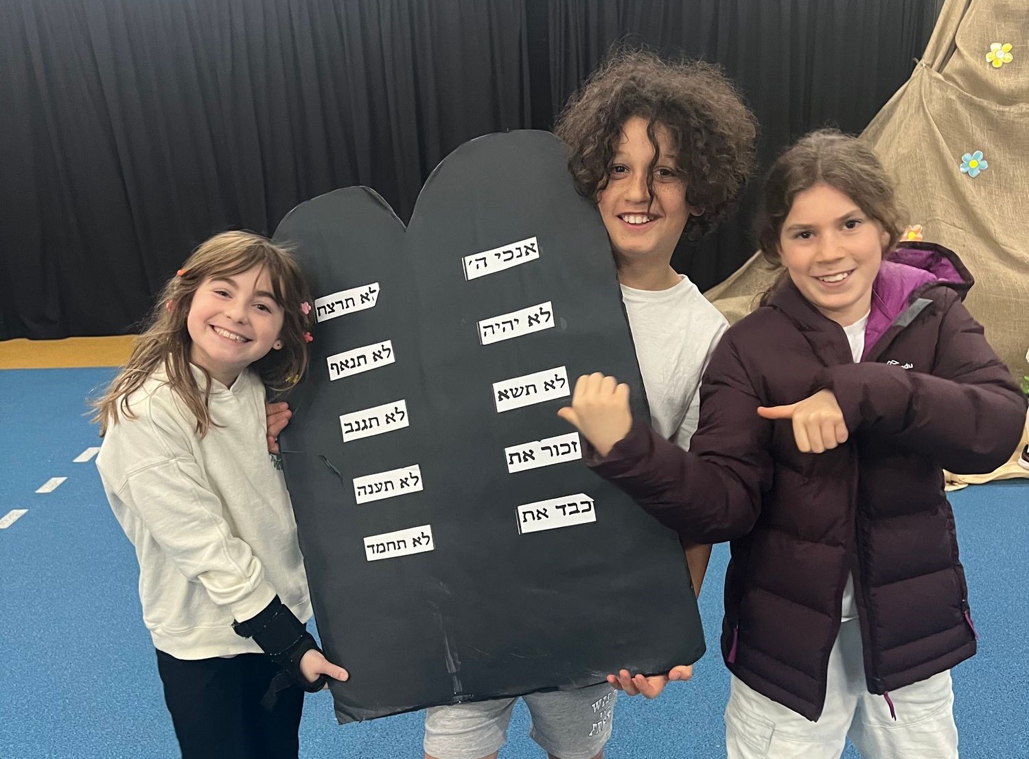 Three students are in front of a replica of Har Sinai, holding the 10 Commandments