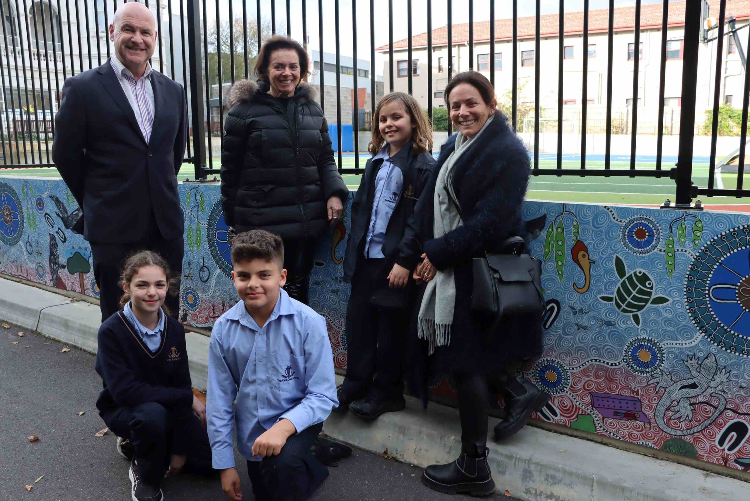 Three students and three adults stand in front of the new First Nations mural at the Dandenong Rd campus, they are looking at the camera and smiling
