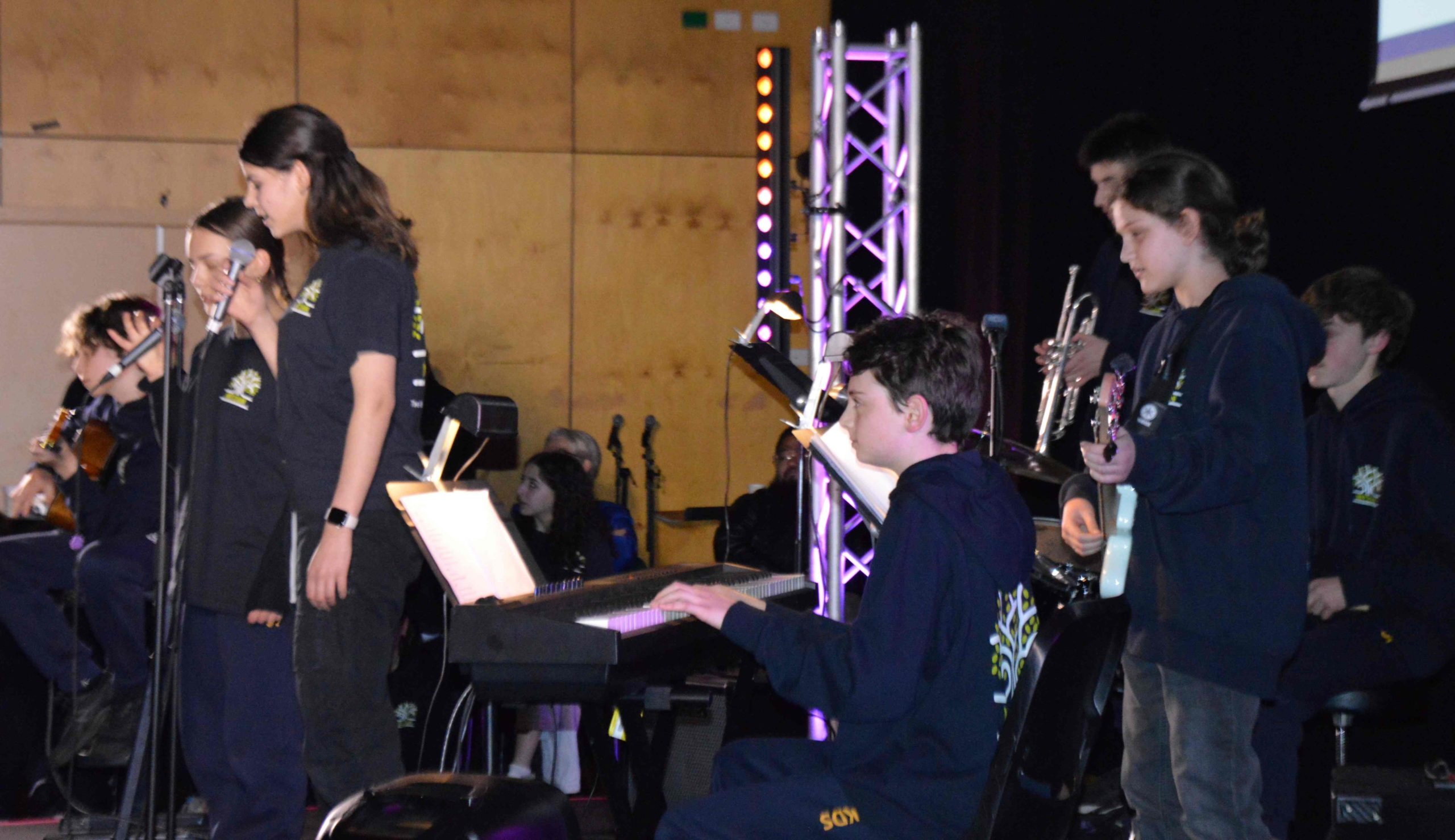 Year 9 students perform an original song they wrote in response to war. They are on a stage with professional lighting.