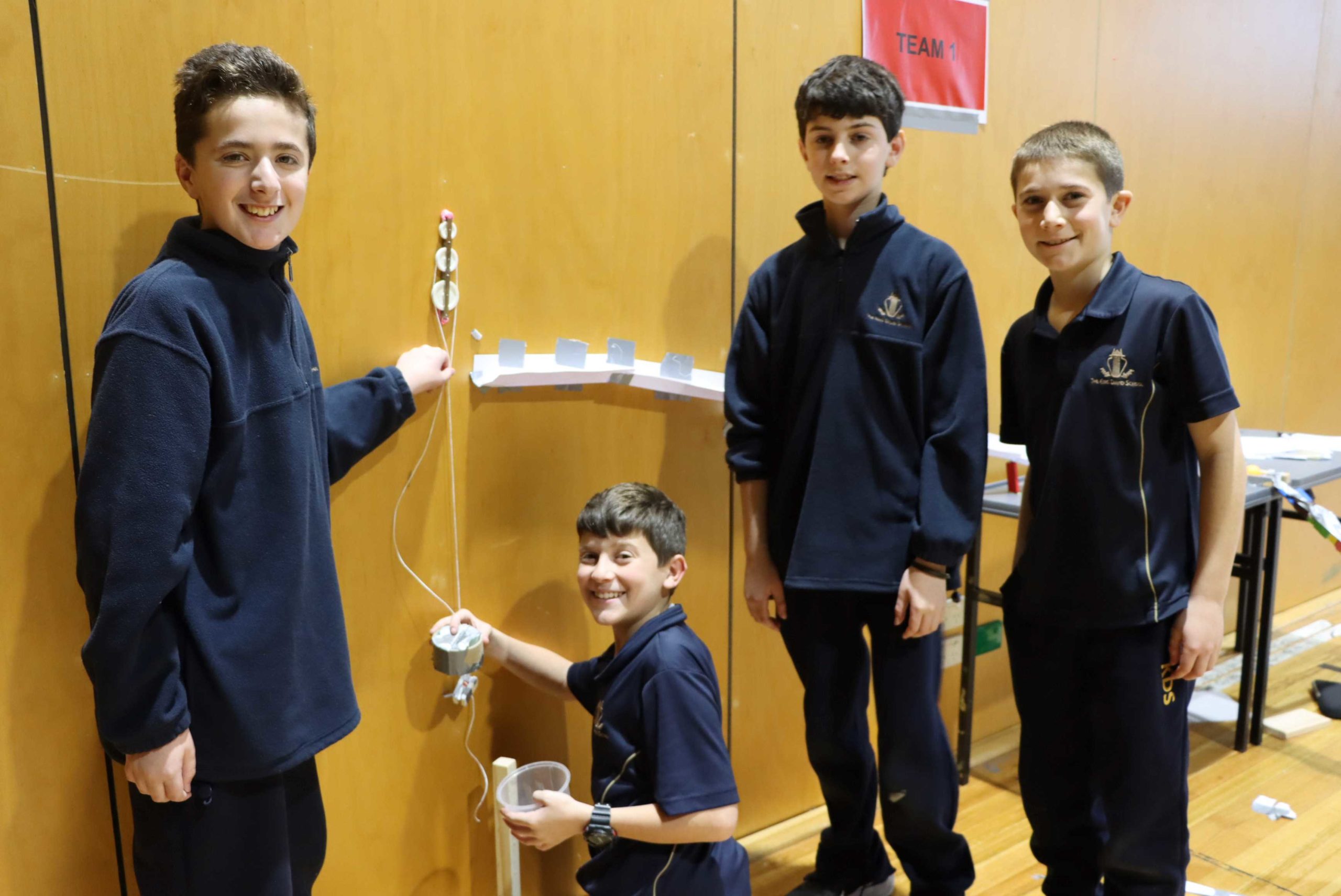 Four Year 7 students are posing in front of their handmade Rube Goldberg machine. They are participating in Project Slingshot - Project-based learning in Year 7