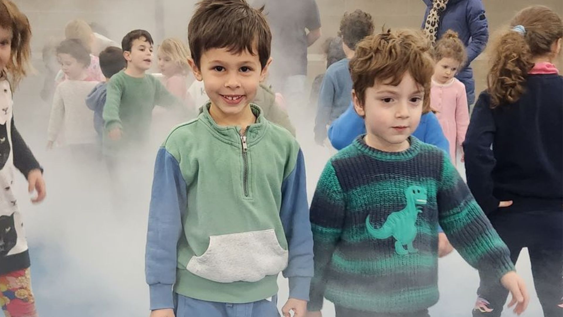Two ELC students face the camera, smiling. They are surrounded by smoke which has been made with water. They are learning about smoke for Science Week