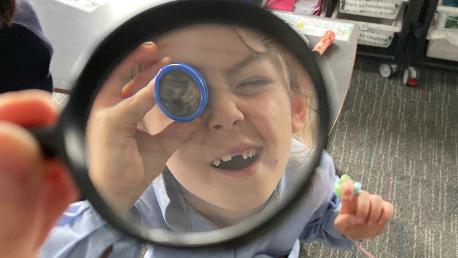 A Year 1 student holds a magnifying glass up to their eye, examining light