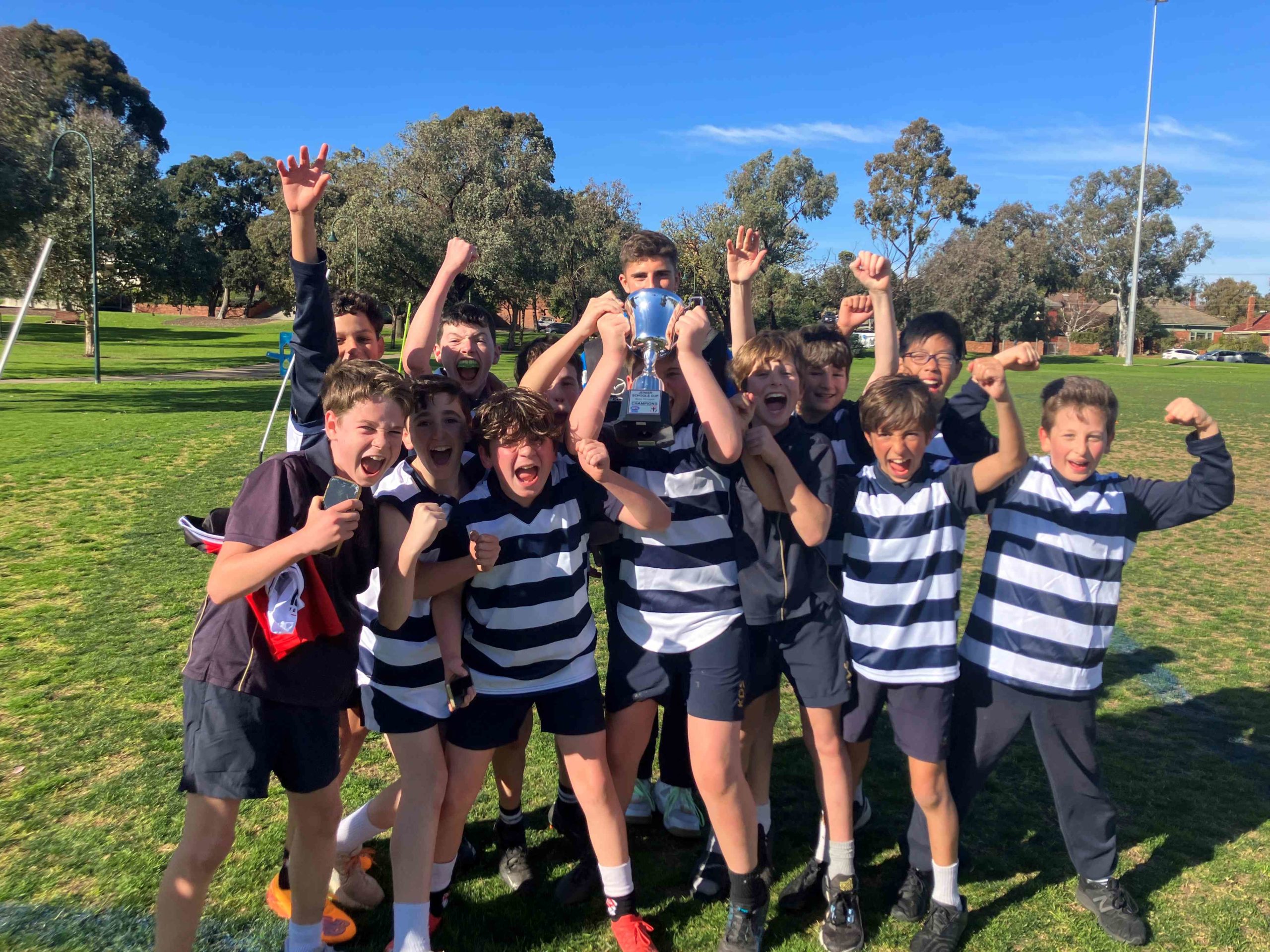 Our Year 6 boys are cheering, with their arms in the air. One boy in the middle is holding a trophy. they have just won the Jewish Schools' 9s AFL Cup.