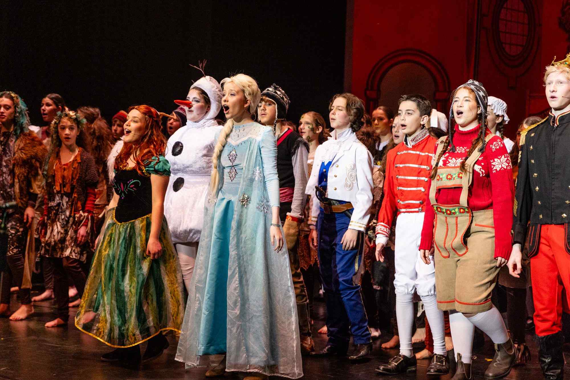 The cast of Frozen Jr, our Years 6-9 musical are on stage in costume. They are singing. The characters of Elsa and Anna are in front.