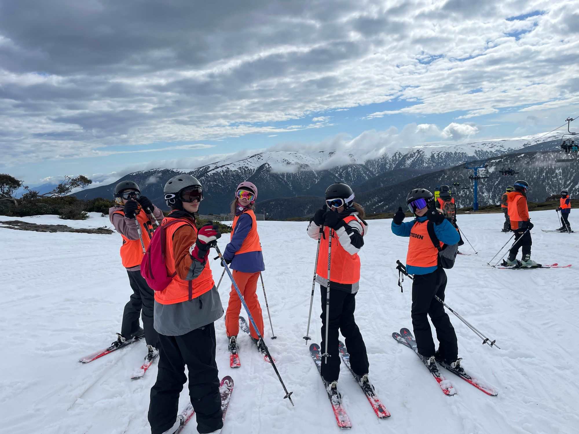 Years 7-10 students are gathered at Falls Creek, they are on skis and are wearing snow clothes. They are looking back at the camera and smiling.
