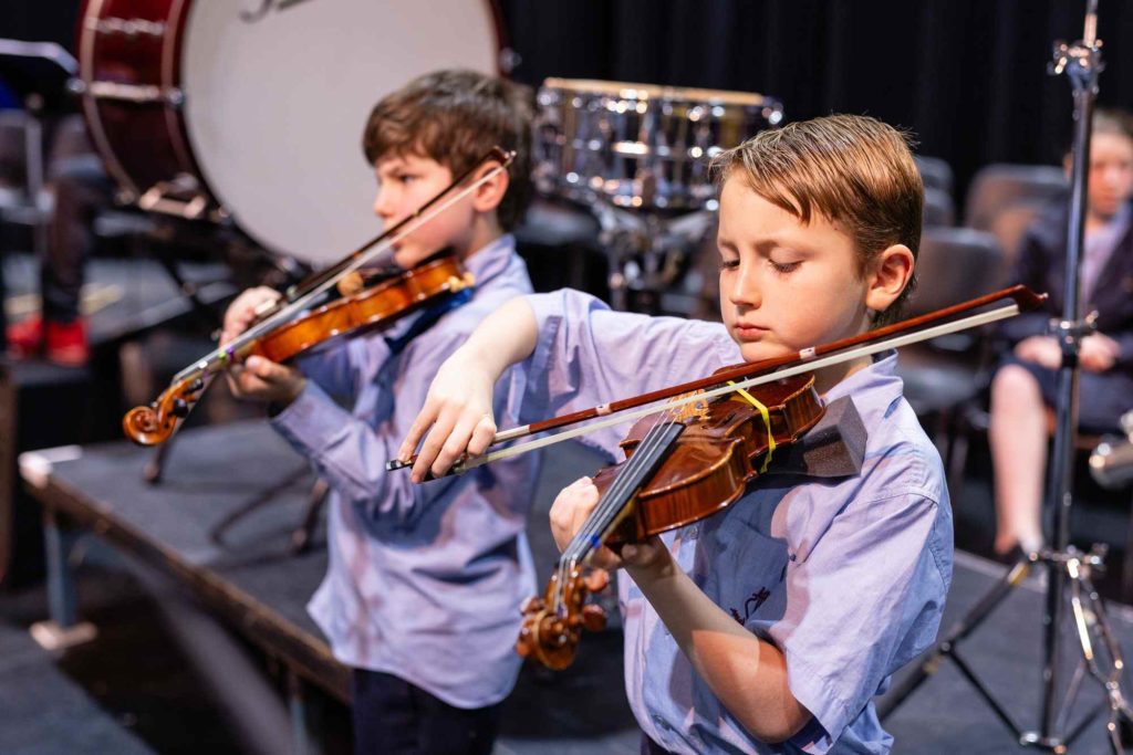 Two Junior School students play the violin at our Spring Concert, they are looking down, concentrating on their playing.