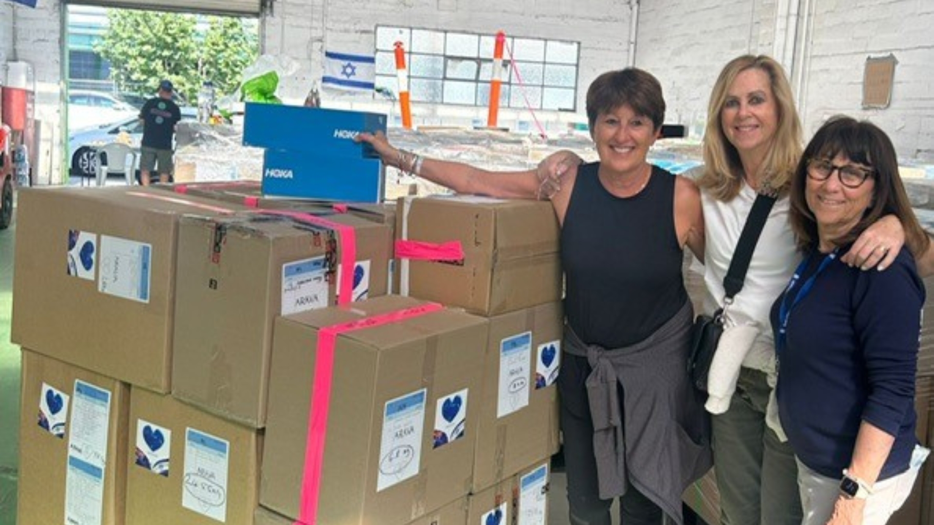 Three smiling women stand in front of boxes of stationery collected by King David students as they arrive in Israel.