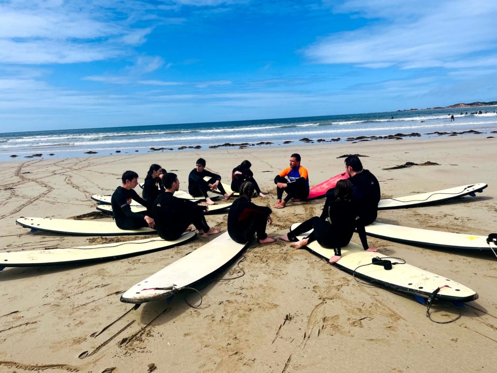 Some of our Year 10 students are sitting on surf boards, in a circle with their surf boards facing inwards. They are facing each other and wearing wetsuits. They are on Year 10 camp - Tiyul b'Yam