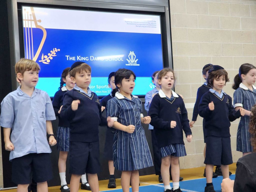 A group of Year 2 students are singing in Hebrew at the Prep-Year 3 Hebrew Assembly and T'filah. They are wearing school uniform.