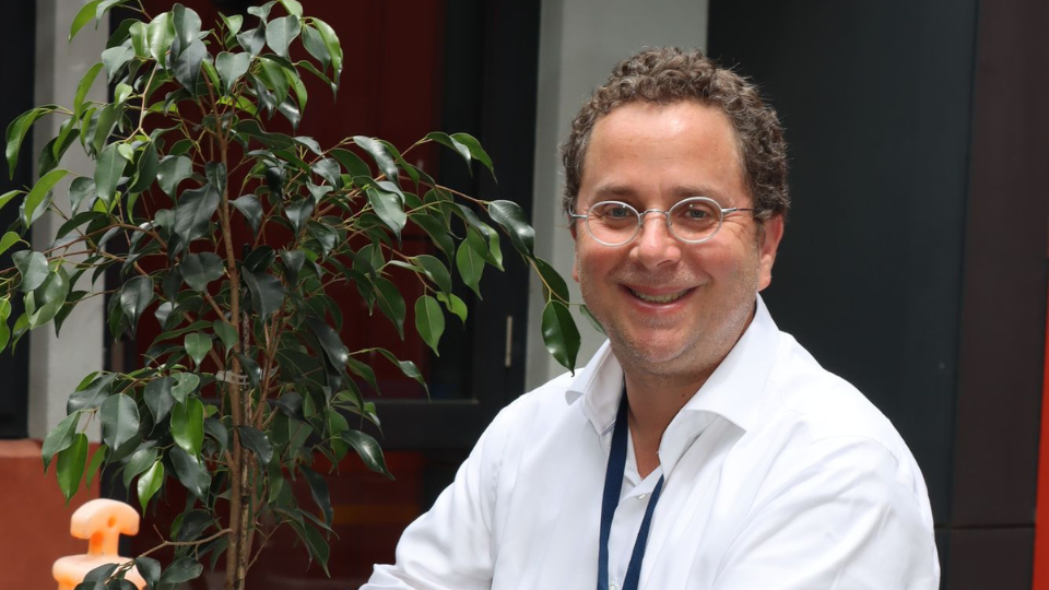Director of Jewish Life and Learning Ilan Bloch is smiling next to a Fig tree that he is planting.
