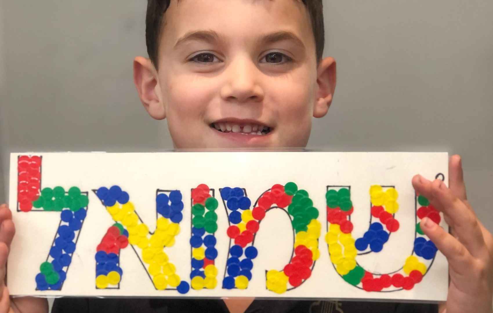 A Prep student holds a sign with his name in Hebrew. It is decorated with colourful stickers.