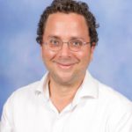 This shows our Director of Jewish Life and Learning, Ilan Bloch, looking at the camera and smiling. He is wearing blue glasses and a white shirt.