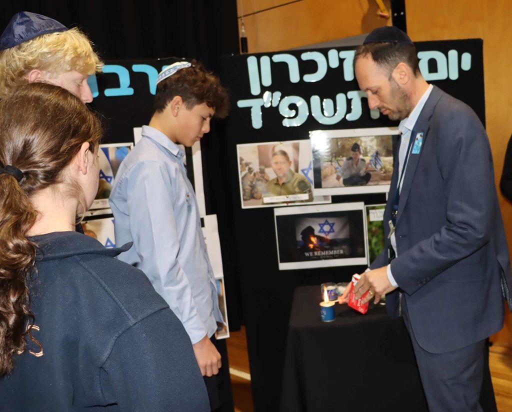 Marc Light and students light memorial candles for Yom HaZikaron. They stand next to photos of soldiers who have died in the recent war. They are solemn.