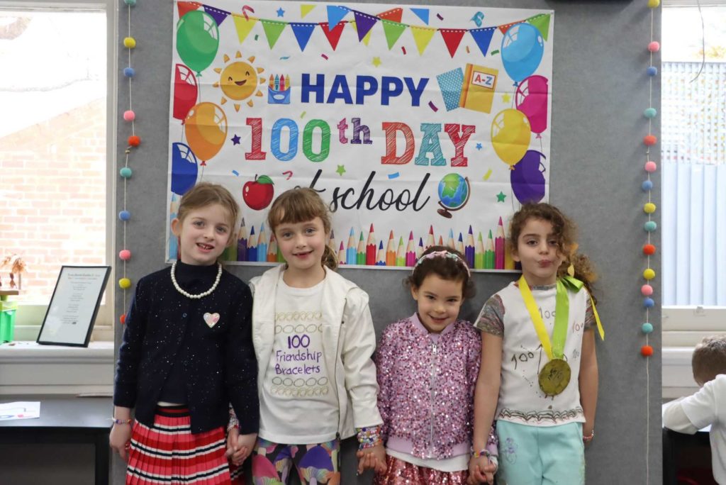 Four Prep students stand smiling in front of a sign with balloons that says Happy 100 days of school. They are dressed as older people.