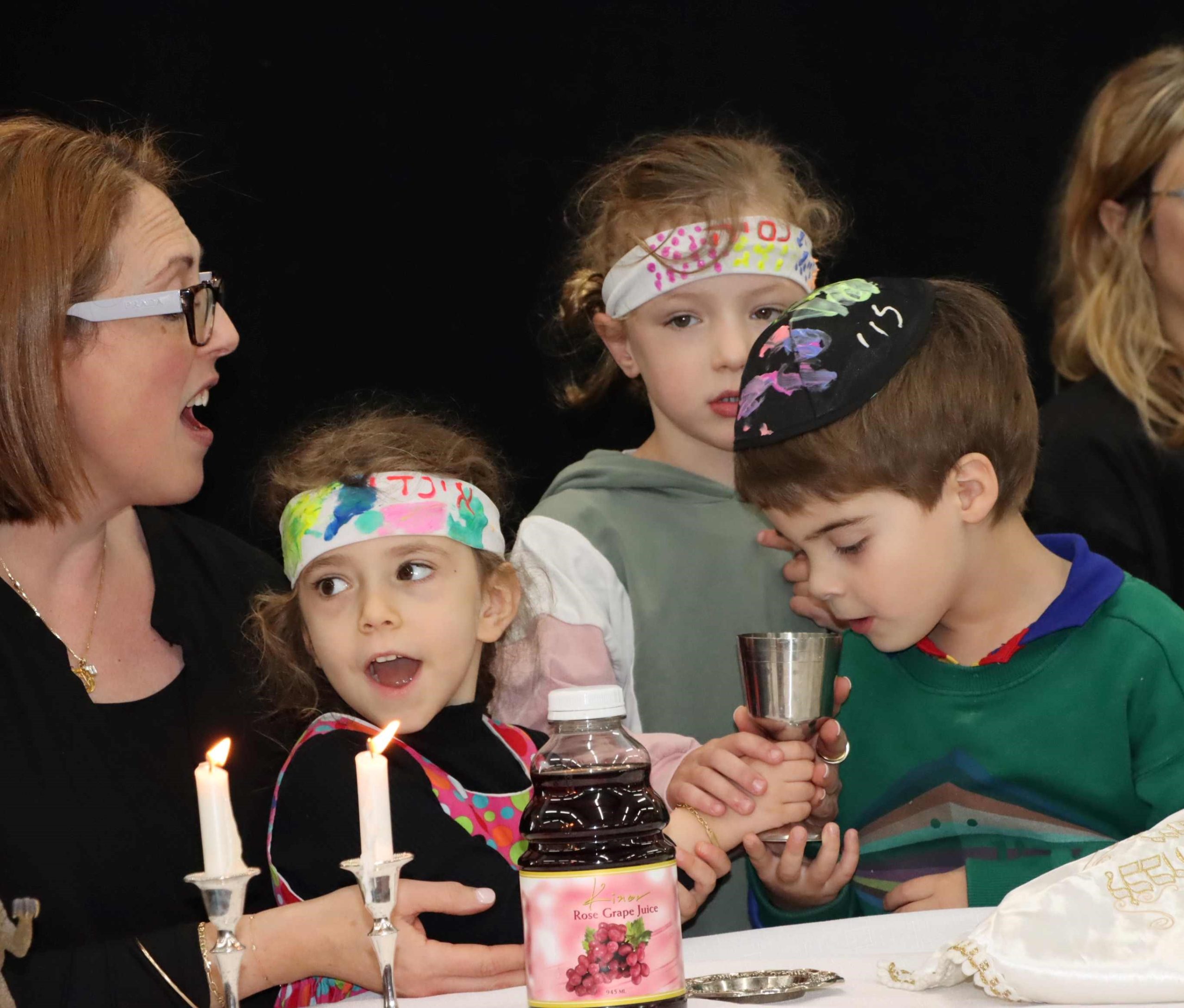ELC Students are smelling kiddush wine and holding a kiddush cup. They are celebrating the Senior Kindergarten Grandparents' and Special Friends Shabbat.