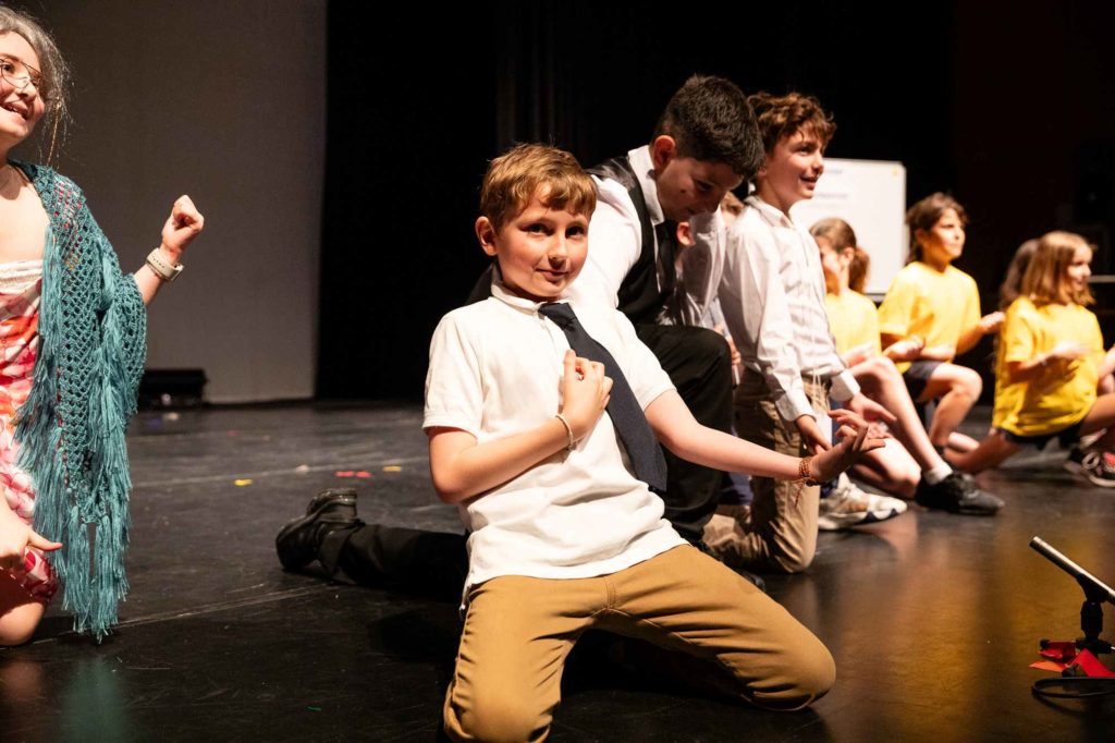 Years 3-5 students are on stage wearing shirts and ties. They are dancing and singing as part of the production, Back from the Future