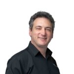 Joshua Samuel is facing the camera. He is attempting to smile. He is wearing a black shirt. We can see from his mid-chest to the top of his head.