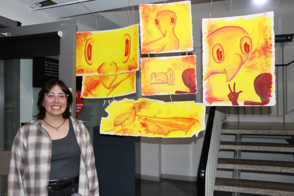 Year 12 student stands in front of her VCE Art making and exhibiting work. The work is yellow and red. She is smiling proudly.