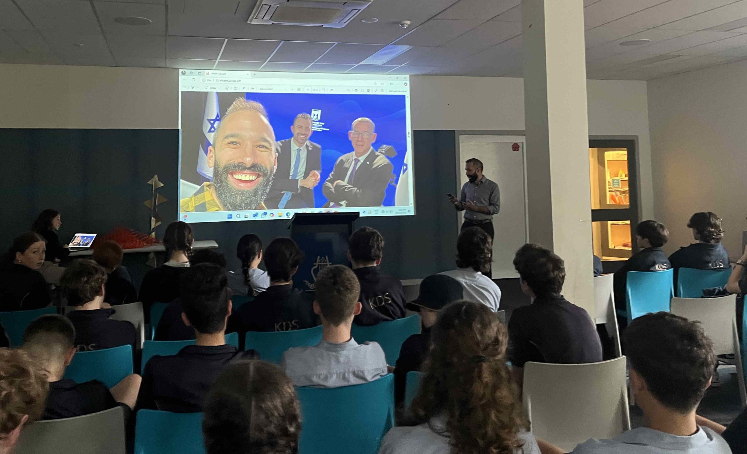 Eli Parkes speaks to Year 8 students in front of a picture of himself with Israeli dignitaries.