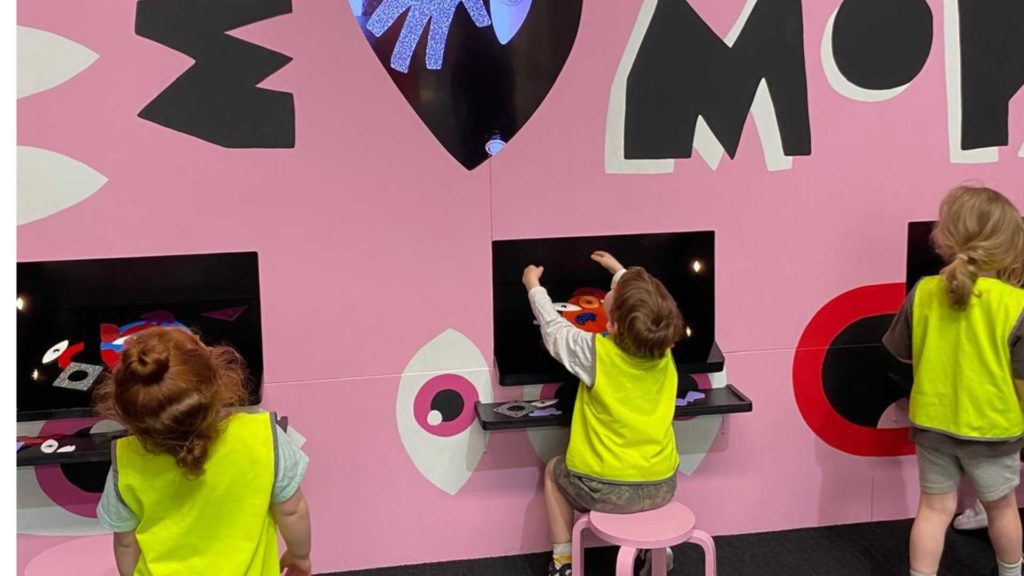 The children of Gan Gefen ELC play at the pink wall at MoPA. They are wearing reflective vests so they don't get lost.
