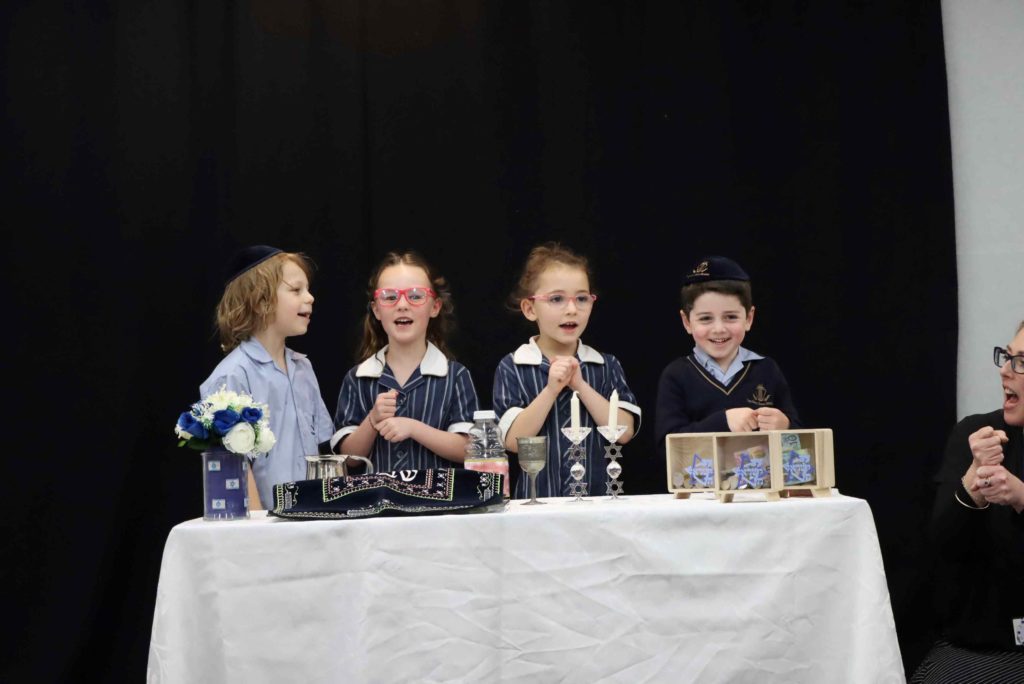 Four Prep students are at the Shabbat table with Shabbat candles, kiddush and challah. They are celebrating Shabbat with their Grandparents and Special Friends.