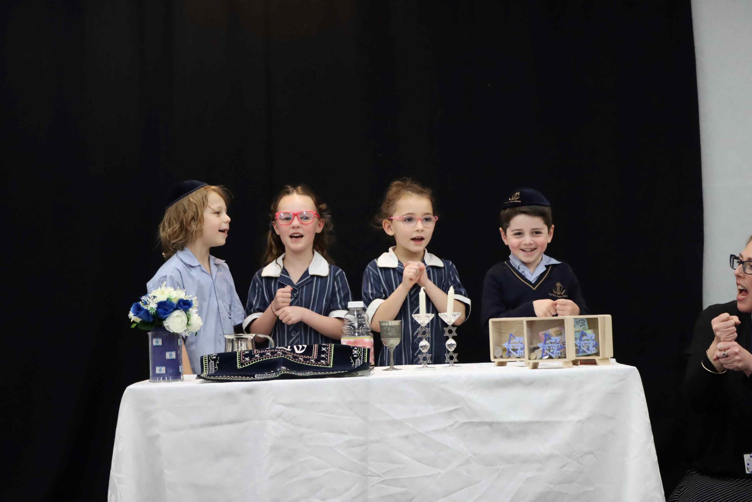 Four Prep students are at the Shabbat table with Shabbat candles, kiddush and challah. They are celebrating Shabbat with their Grandparents and Special Friends.