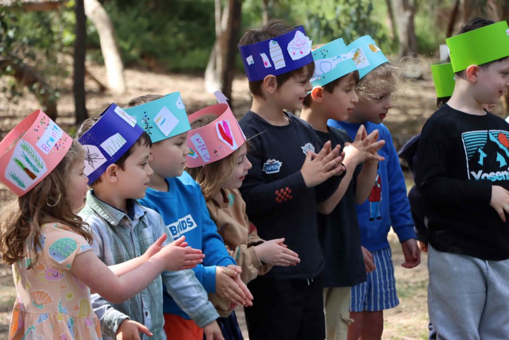 Our Senior Kinder students are excitedly celebrating the end of Kinder at the Urban Forest. They are wearing colourful paper crowns they decorated themselves.
