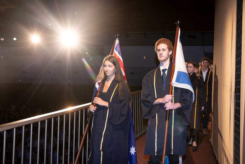 Students from the Class of 2024 are wearing Graduation gowns. they are carrying the Australian and the Israeli flags at Presentation Evening.