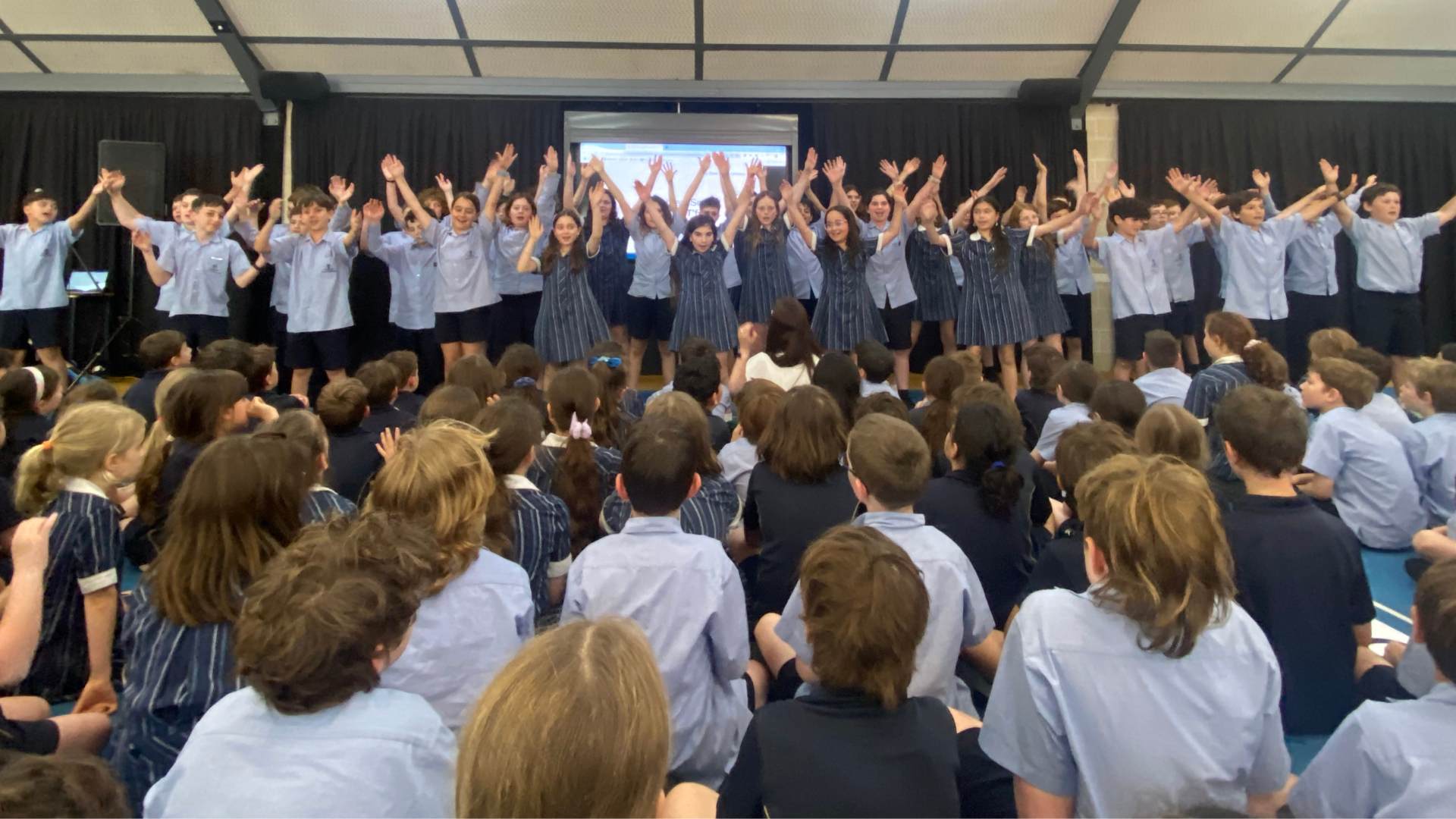 Year 5 students are singing with their arms in the air. They are celebrating finishing at our Dandenong Road Campus. They will move to the Magid Campus for Year 6.