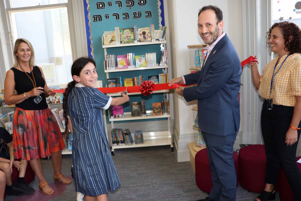 Principal Marc Light is cutting a red ribbon with a Year 5 student. they are officially opening the Hebrew section of the Dandenong Rd Campus library.