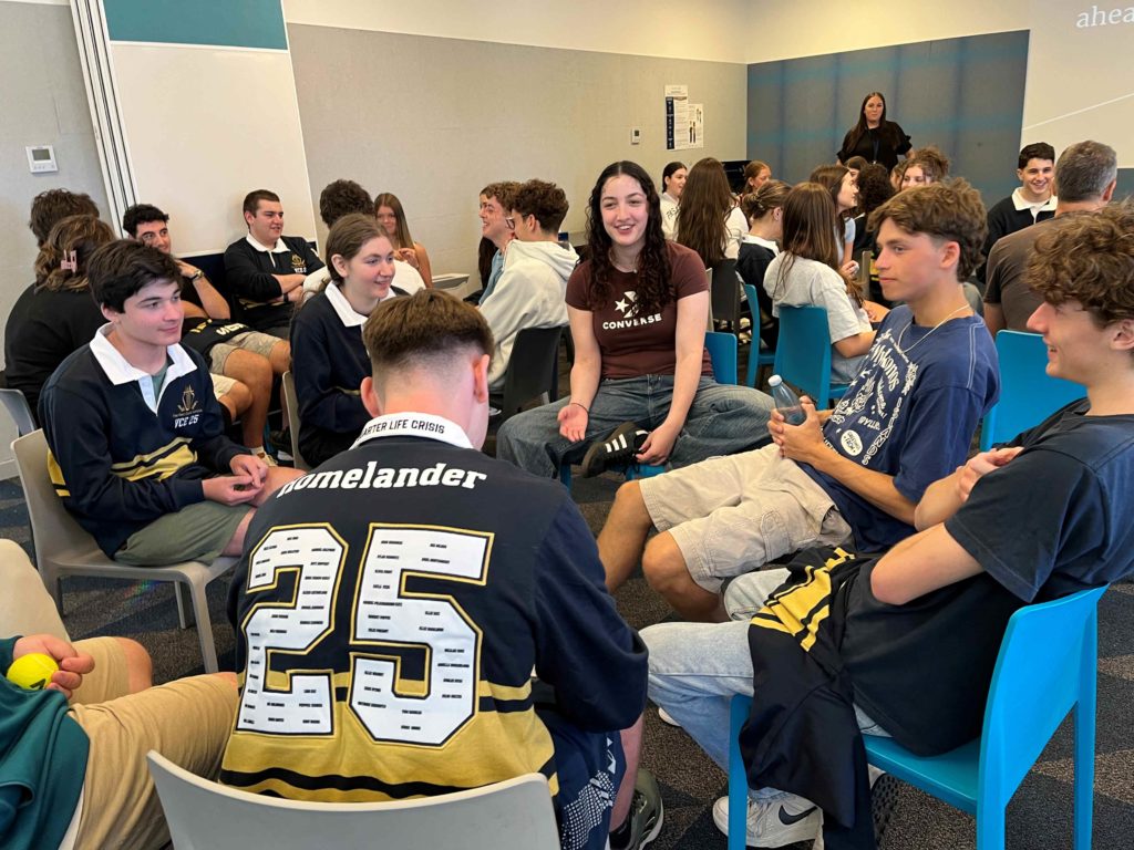 Year 12 students are talking with alumni on their first day of Year 12. Alumni have returned to school to give them tips about VCE. They are dressed in casual clothes with some in their new Year 12 2025 VCE Jerseys.