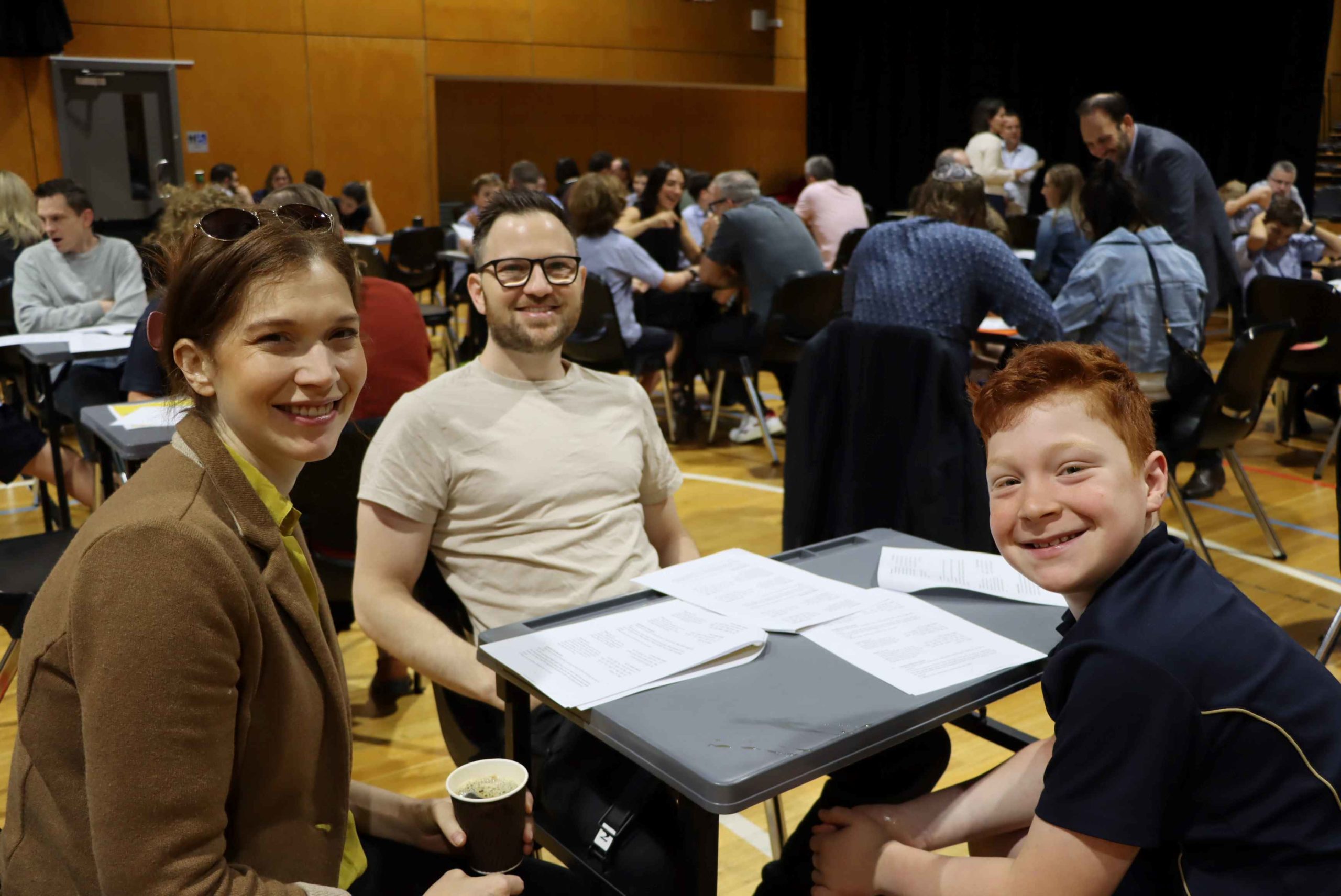 A Year 6 student in uniform is with his parents. They are learning Pirkei Avot together to celebrate Yom HaMishpachah - Family Day, They are happy.