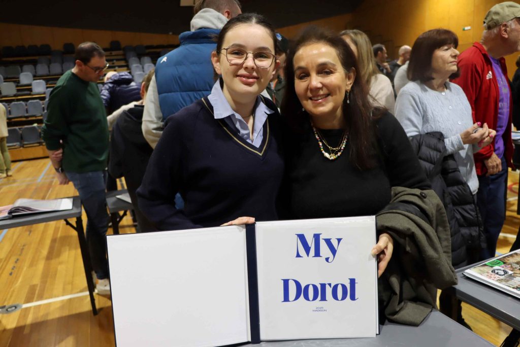 A Year 8 student stands with her mother, behind her Dorot project book that tells her family history.