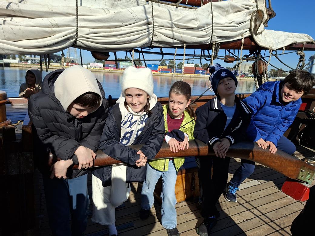 Year 4 students are wearing warm jackets and beanies. They are outside, on the deck of the 1830s replica sailing ship, The Enterprize. They are learning about the First Fleet and the colonisation of Melbourne.